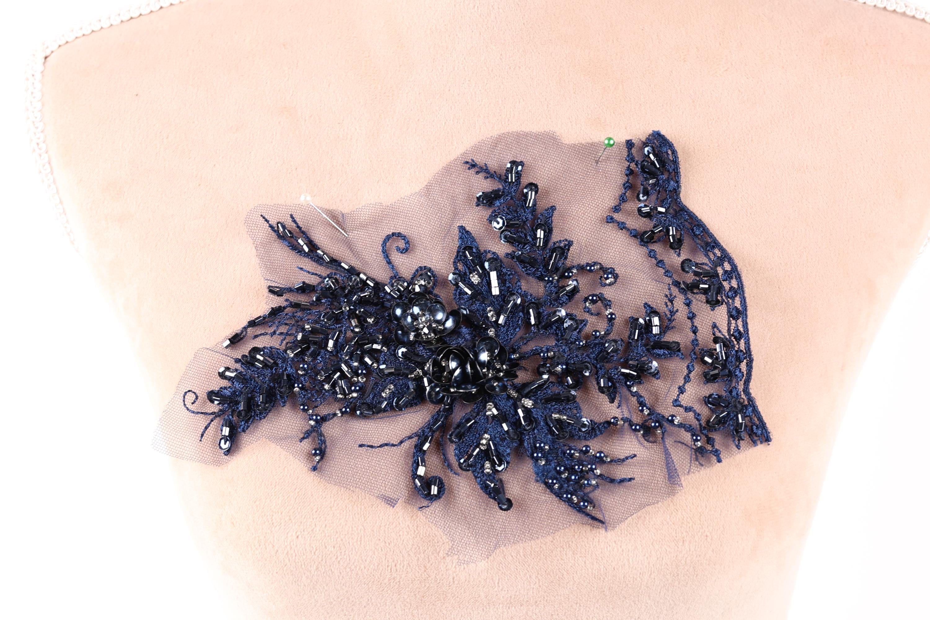 a close-up view of a piece of fabric with a decorative element, possibly a lace or embroidery piece, featuring a variety of blue and black beads or sequins.