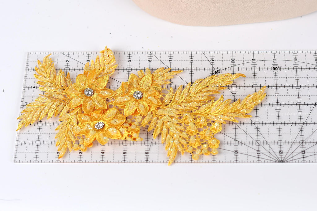 a close-up view of a piece of fabric with gold glitter leaves and flowers attached to it, placed on a ruler for scale.