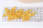 a close-up view of a piece of fabric with gold glitter leaves and flowers attached to it, placed on a ruler for scale.