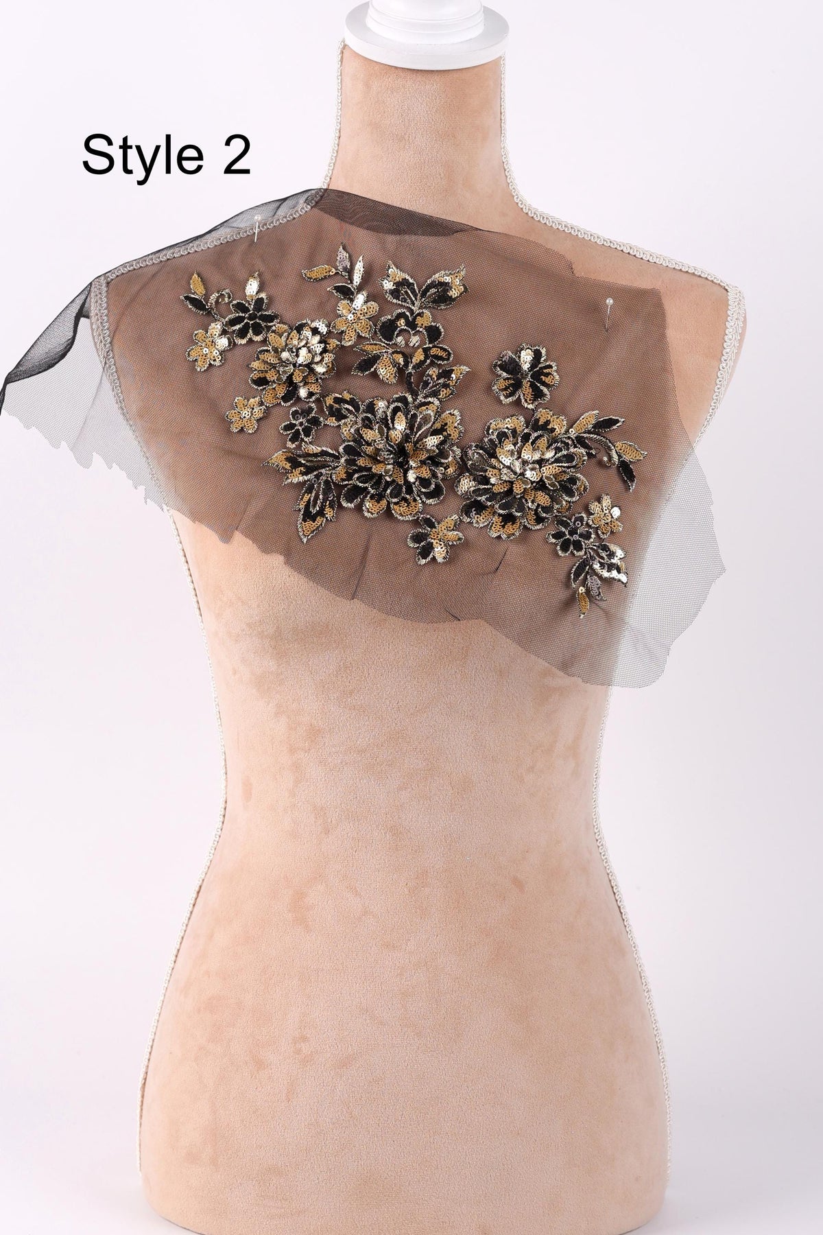 A mannequin with a decorative fabric piece on its shoulder, featuring a floral pattern in black and gold colors.