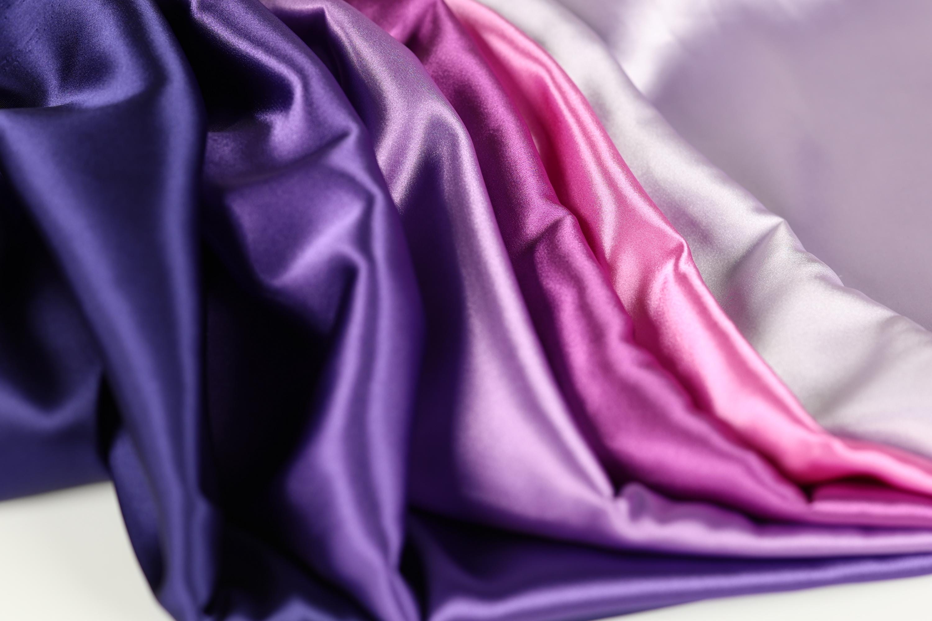 a close-up view of a fabric with a variety of colors, including purple, pink, and white. The fabric appears to be folded or crumpled, creating a visually interesting texture.