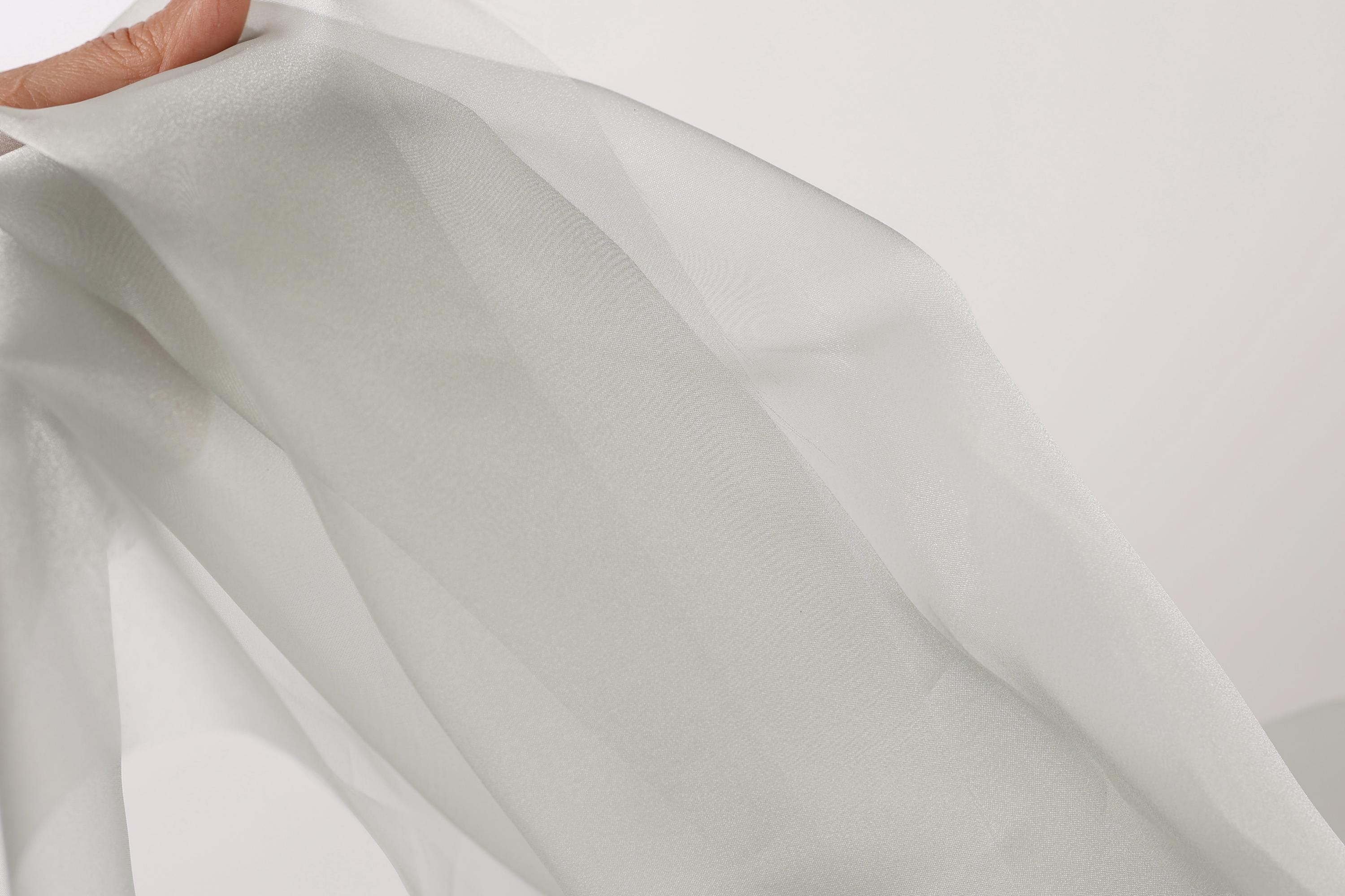 A hand is holding a piece of white fabric, which appears to be a sheer or sheer-like material.