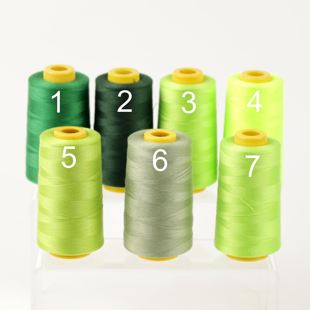 six spools of thread in various colors, including green, yellow, and gray, arranged in a row.