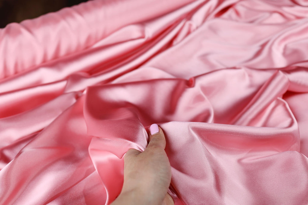 a person is sewing a pink satin material