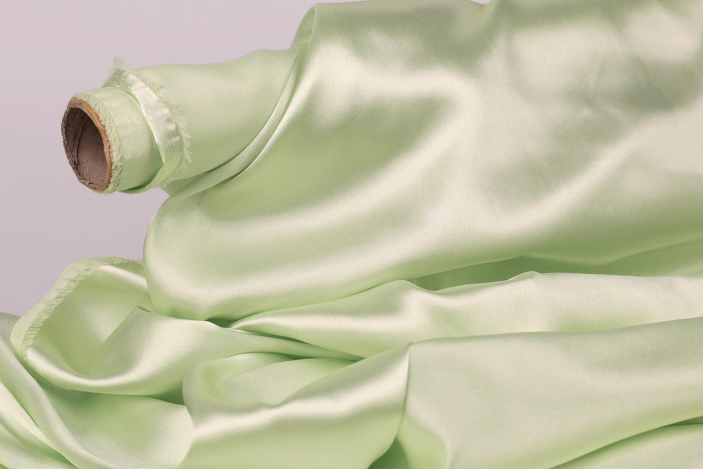A close-up view of a piece of green satin fabric, with its smooth and shiny surface visible.