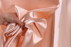 A hand is holding a piece of peach-colored satin fabric, which appears to be a bow or ribbon.