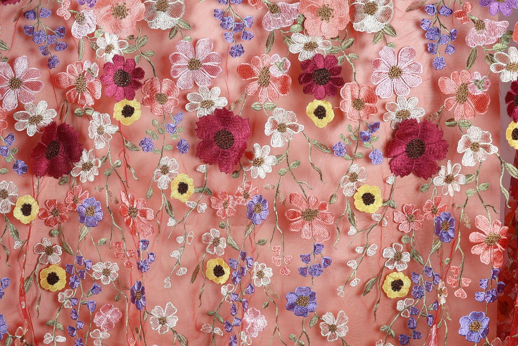 a close-up view of a fabric with a vibrant floral pattern. The fabric is adorned with a variety of colorful flowers, including red, pink, yellow, and purple, arranged in a visually appealing manner. The flowers are intricately embroidered or stitched onto the fabric, creating a lively and eye-catching design.