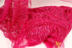 a close-up view of a vibrant pink fabric with a sparkling, sequined texture. The fabric appears to be a sheer or sheer-like material, with a delicate and intricate design. The background is a plain white surface, which allows the pink fabric to stand out prominently.