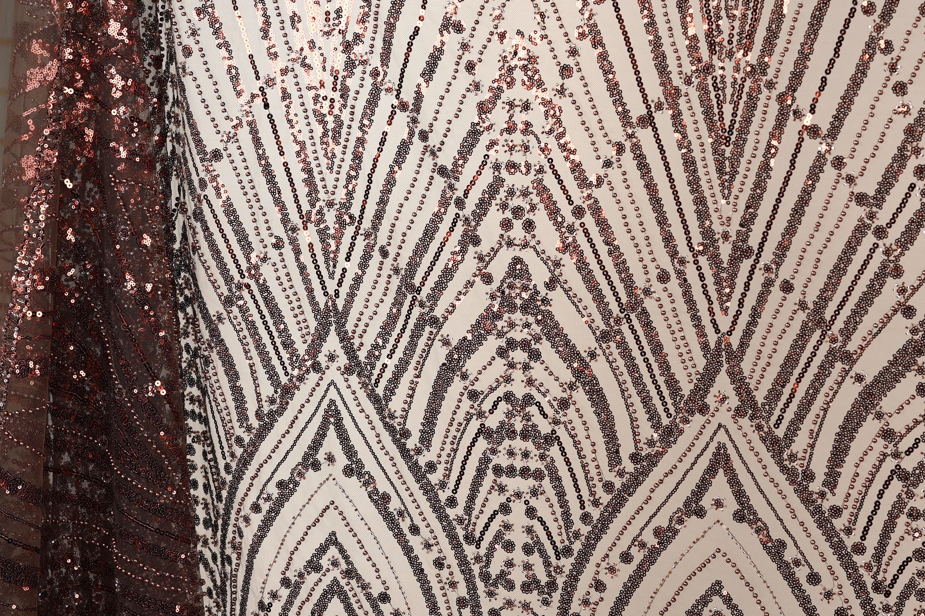 a close-up view of a fabric with a repeating pattern of sequin designs in shades of brown and black. The pattern appears to be a geometric design with a repeating diamond shape and lines, creating a visually striking and intricate design.