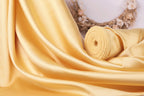 a close-up view of a yellow fabric, possibly silk or satin, with a wreath of flowers in the background.