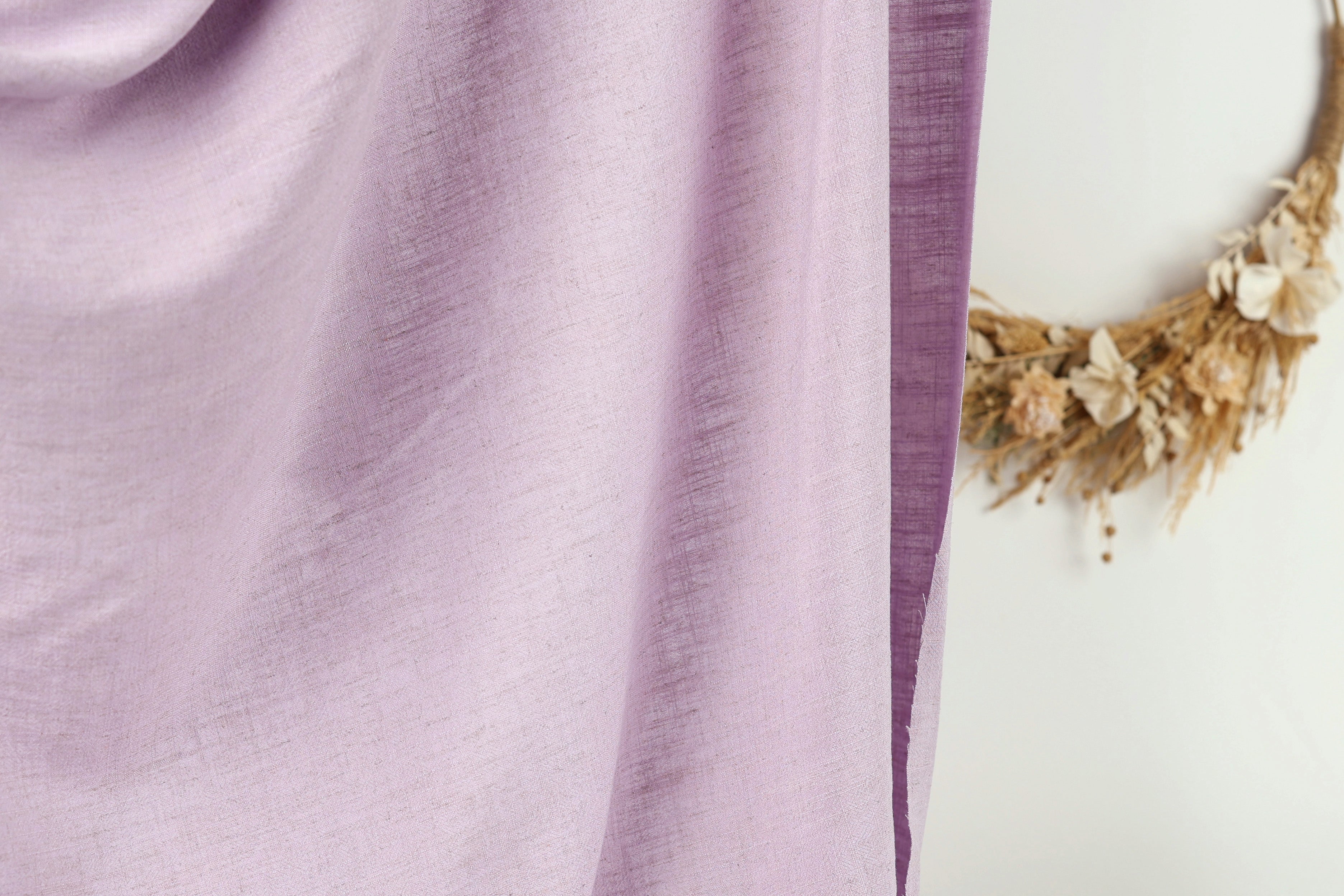 a close-up view of a purple fabric, with a wreath of dried flowers hanging on a wall in the background.