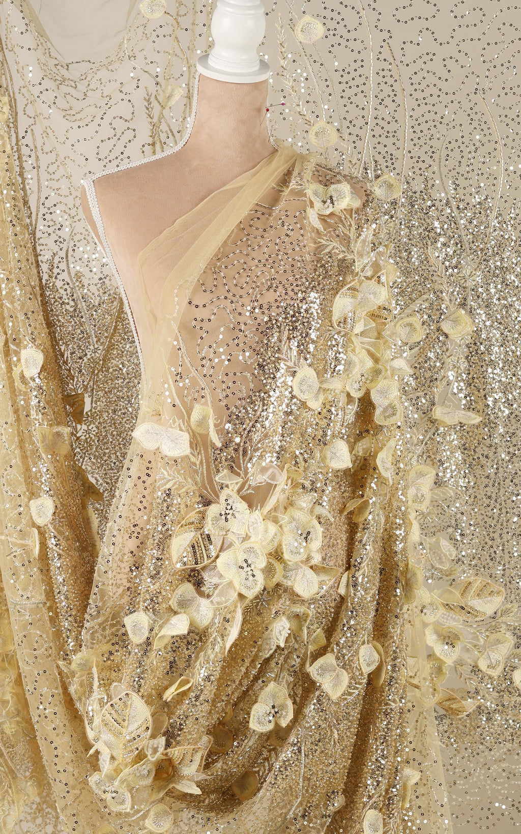 a mannequin wearing a gold sequin dress with a sheer, floral-patterned fabric draped over it.