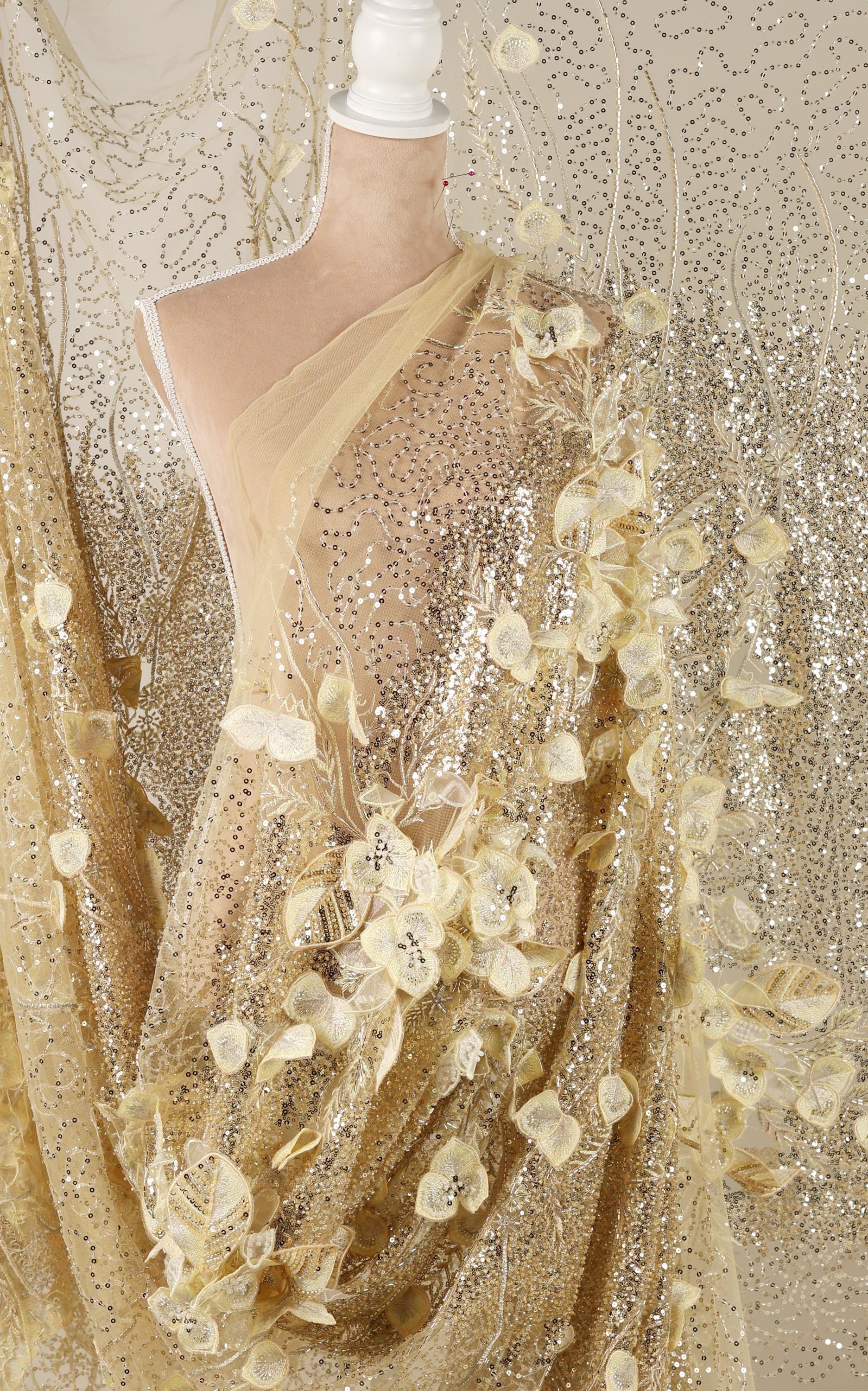 a mannequin wearing a gold sequin dress with a sheer, floral-patterned fabric draped over it.
