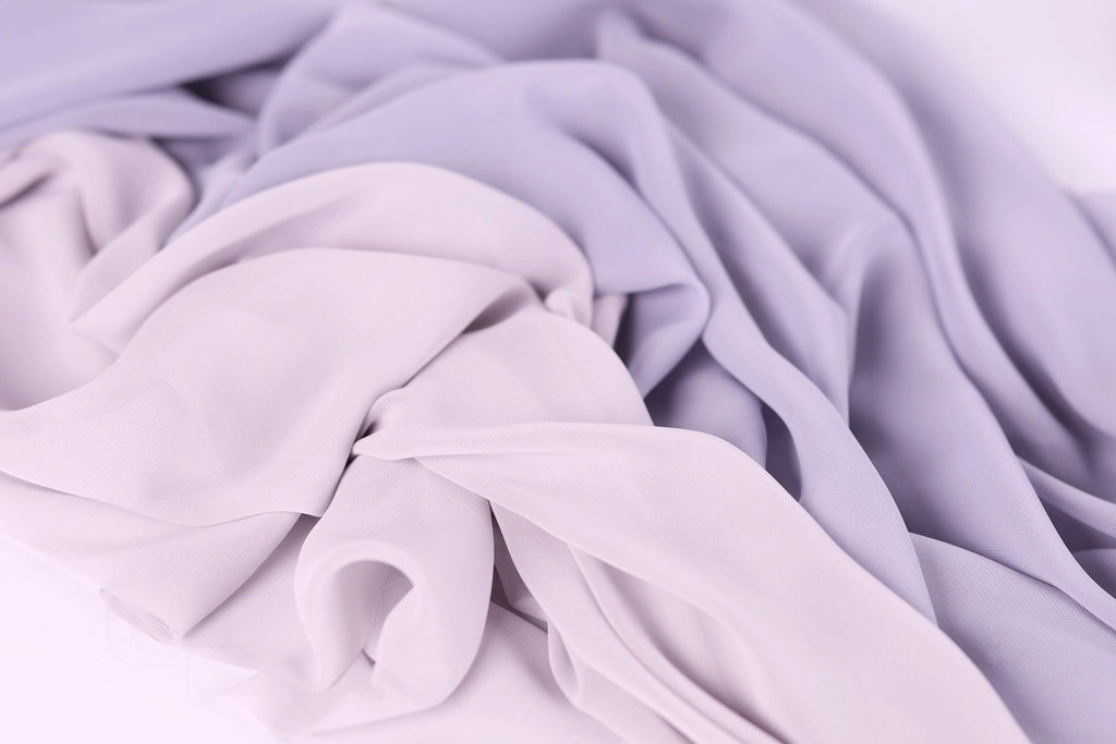 The image is a close-up of a soft, flowing fabric with a mix of lavender and light purple hues. The fabric appears to be made of a sheer, lightweight material, giving it a delicate and airy appearance.
