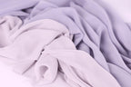 The image is a close-up of a soft, flowing fabric with a mix of lavender and light purple hues. The fabric appears to be made of a sheer, lightweight material, giving it a delicate and airy appearance.