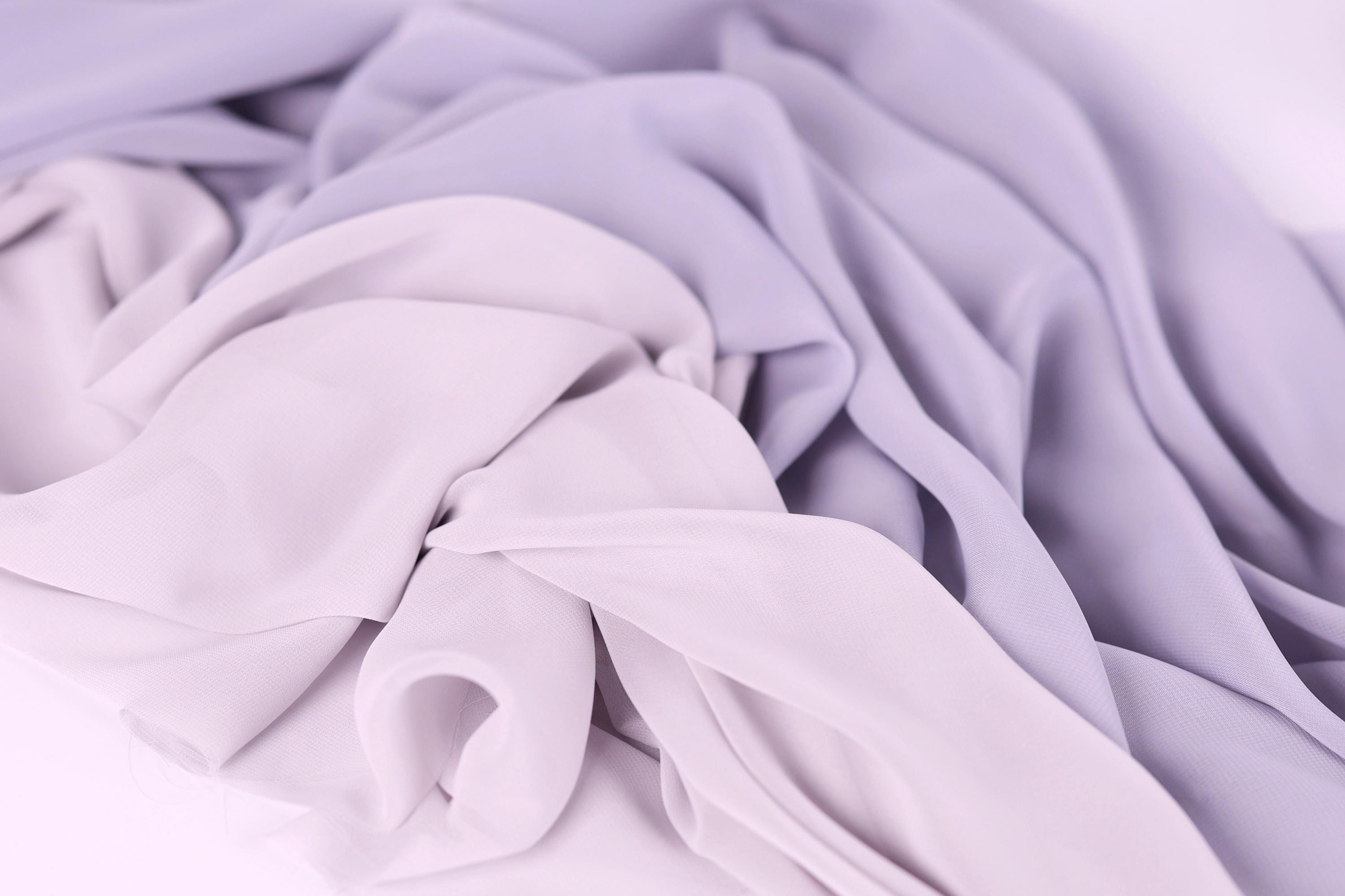 The image is a close-up of a soft, flowing fabric with a mix of lavender and light purple hues. The fabric appears to be made of a sheer, lightweight material, giving it a delicate and airy appearance.