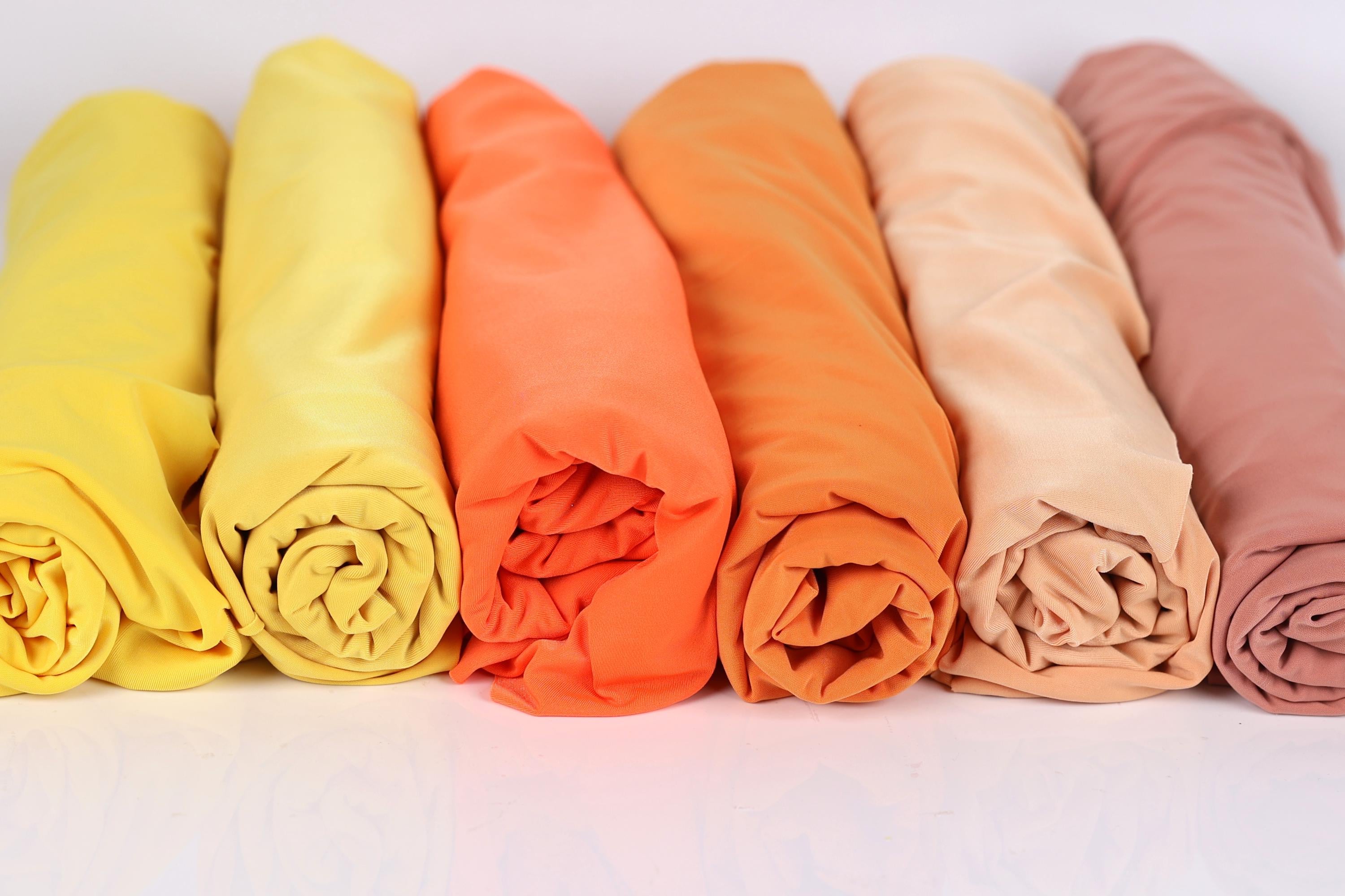A row of six rolled-up fabric pieces in various colors, including yellow, orange, pink, and peach.