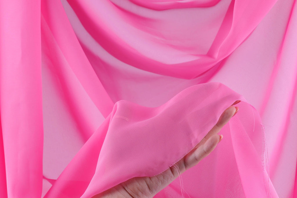 A hand is holding a piece of pink fabric against a background of pink fabric, creating a visually striking contrast.