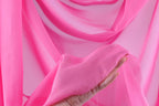 A hand is holding a piece of pink fabric against a background of pink fabric, creating a visually striking contrast.