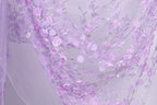 a close-up view of a delicate, intricately designed fabric with a floral pattern. The fabric is predominantly purple, with white accents and delicate pink flowers. The pattern is detailed and detailed, showcasing the craftsmanship and artistry involved in creating this fabric.