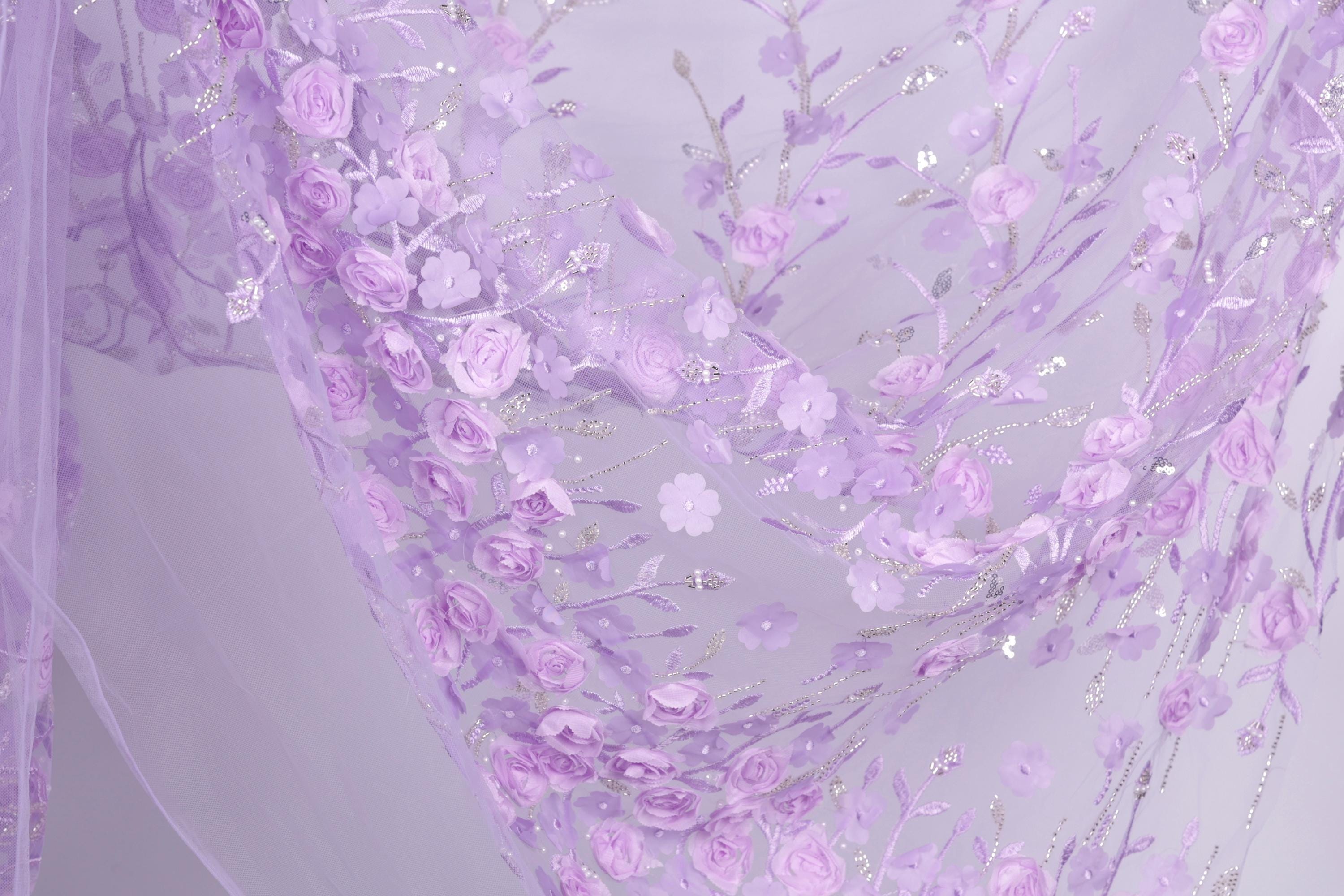 a close-up view of a delicate, intricately designed fabric with a floral pattern. The fabric is predominantly purple, with white accents and delicate pink flowers. The pattern is detailed and detailed, showcasing the craftsmanship and artistry involved in creating this fabric.