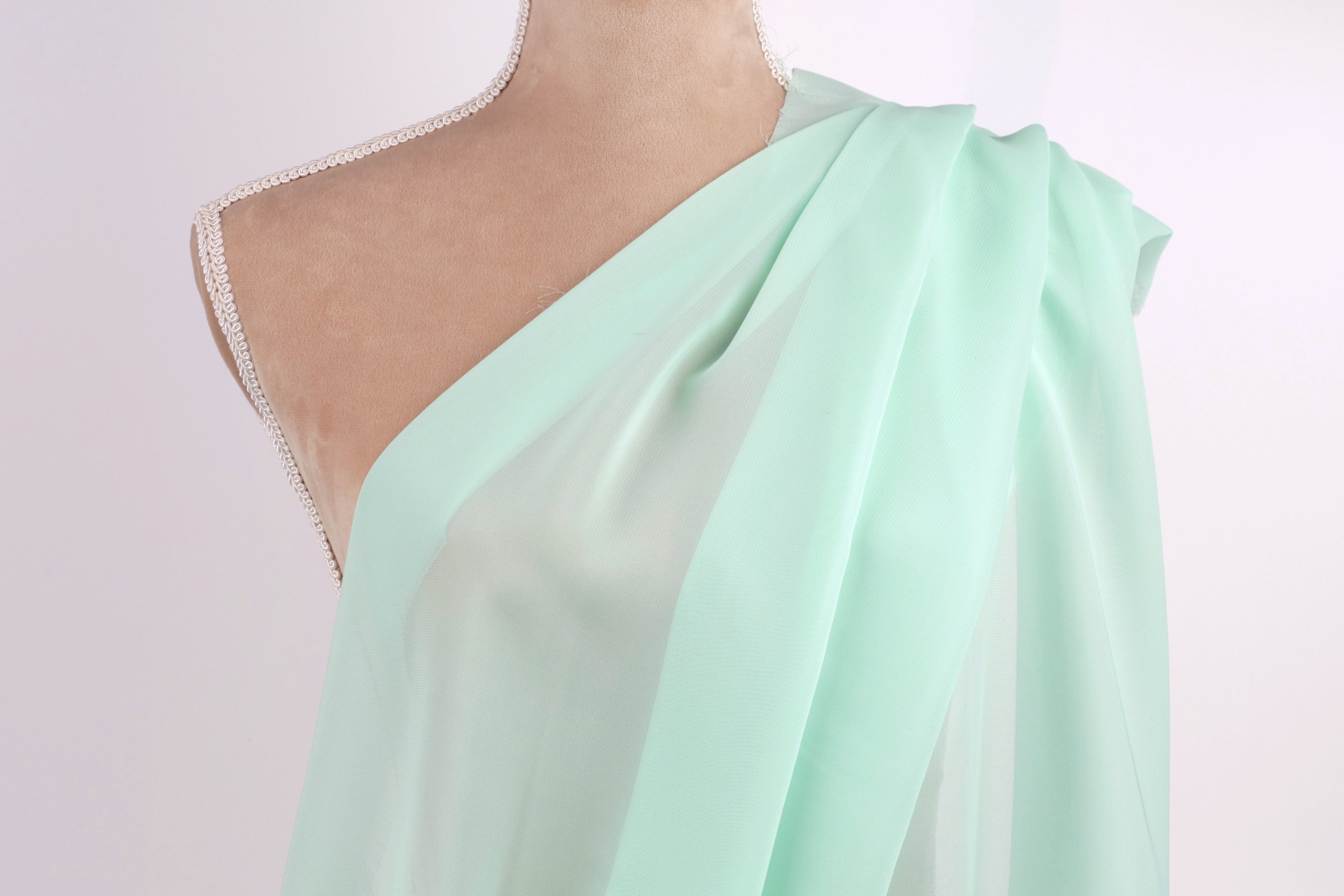 A mannequin wearing a mint green draped dress with a one-shoulder design.
