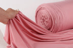 A hand is holding a pink fabric, which appears to be a large roll of the material.