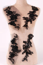 A mannequin torso with black lace appliques or decorations sewn onto it.