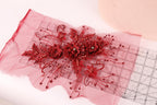 a close-up view of a red floral embroidery on a pink fabric, with a ruler visible in the background.
