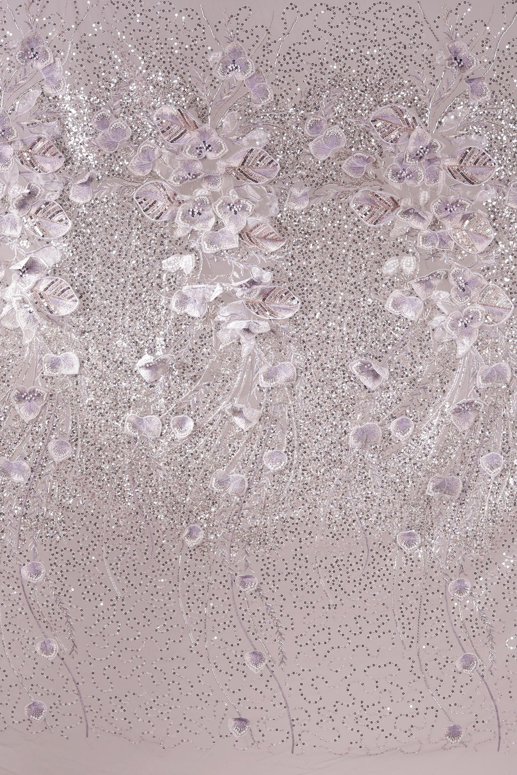 a close-up view of a fabric with a delicate, intricate design of small, white flowers or leaves. The fabric appears to be a light pink color, and the design is composed of numerous small, white flowers or leaves arranged in a repeating pattern across the fabric's surface. The image does not contain any text or other discernible objects, and the focus is solely on the detailed floral design.