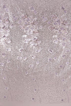 a close-up view of a fabric with a delicate, intricate design of small, white flowers or leaves. The fabric appears to be a light pink color, and the design is composed of numerous small, white flowers or leaves arranged in a repeating pattern across the fabric's surface. The image does not contain any text or other discernible objects, and the focus is solely on the detailed floral design.