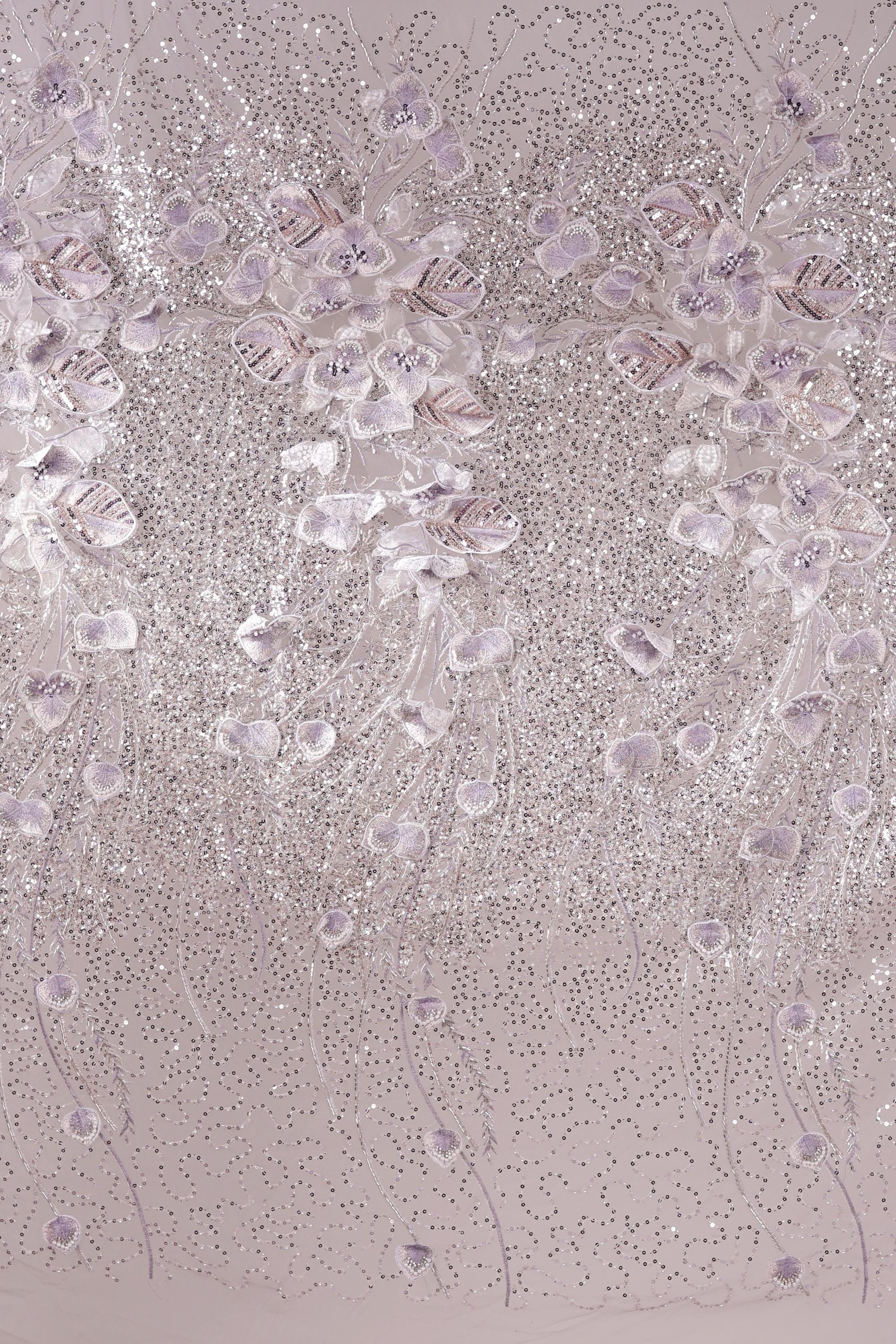 a close-up view of a fabric with a delicate, intricate design of small, white flowers or leaves. The fabric appears to be a light pink color, and the design is composed of numerous small, white flowers or leaves arranged in a repeating pattern across the fabric's surface. The image does not contain any text or other discernible objects, and the focus is solely on the detailed floral design.