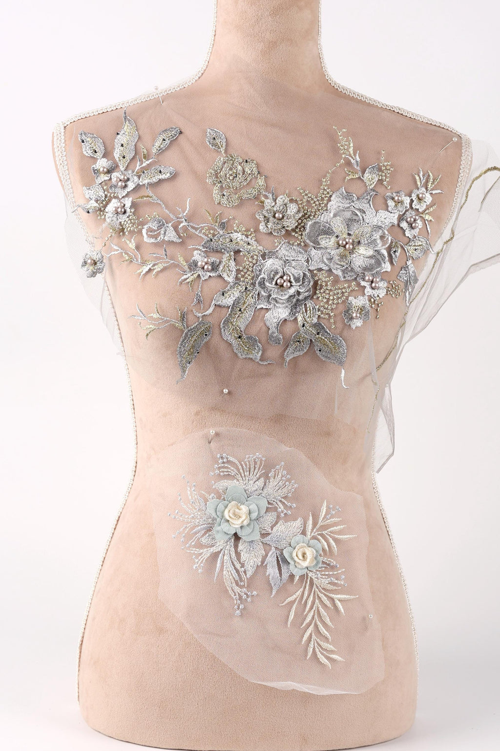 A mannequin with a beige body and a white dress form top, adorned with intricate silver and white floral embroidery.