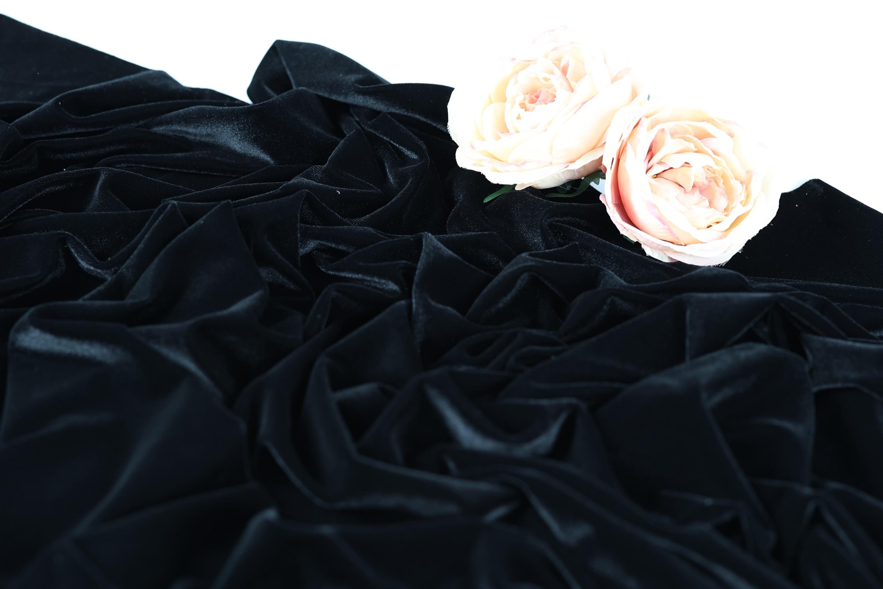 a close-up view of a black velvet fabric with two delicate pink roses resting on top of it.