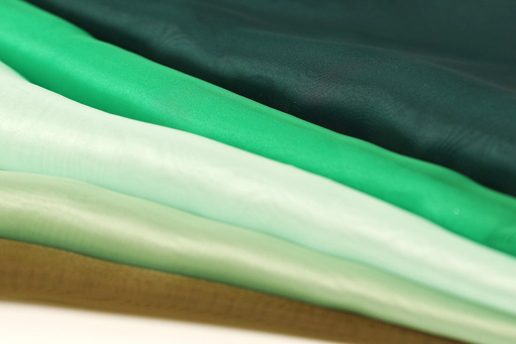 A close-up image of a stack of fabric swatches in various shades of green, ranging from mint to dark green.
