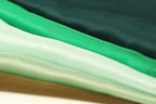 A close-up image of a stack of fabric swatches in various shades of green, ranging from mint to dark green.