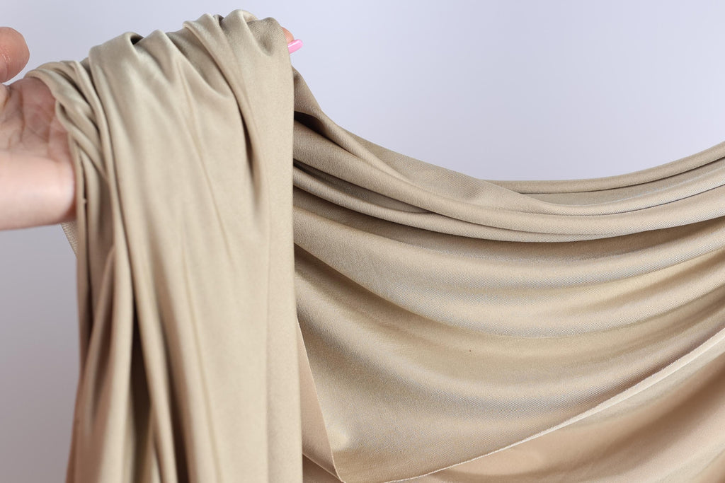 A hand is holding a piece of light brown fabric, which appears to be a type of chiffon or sheer material.