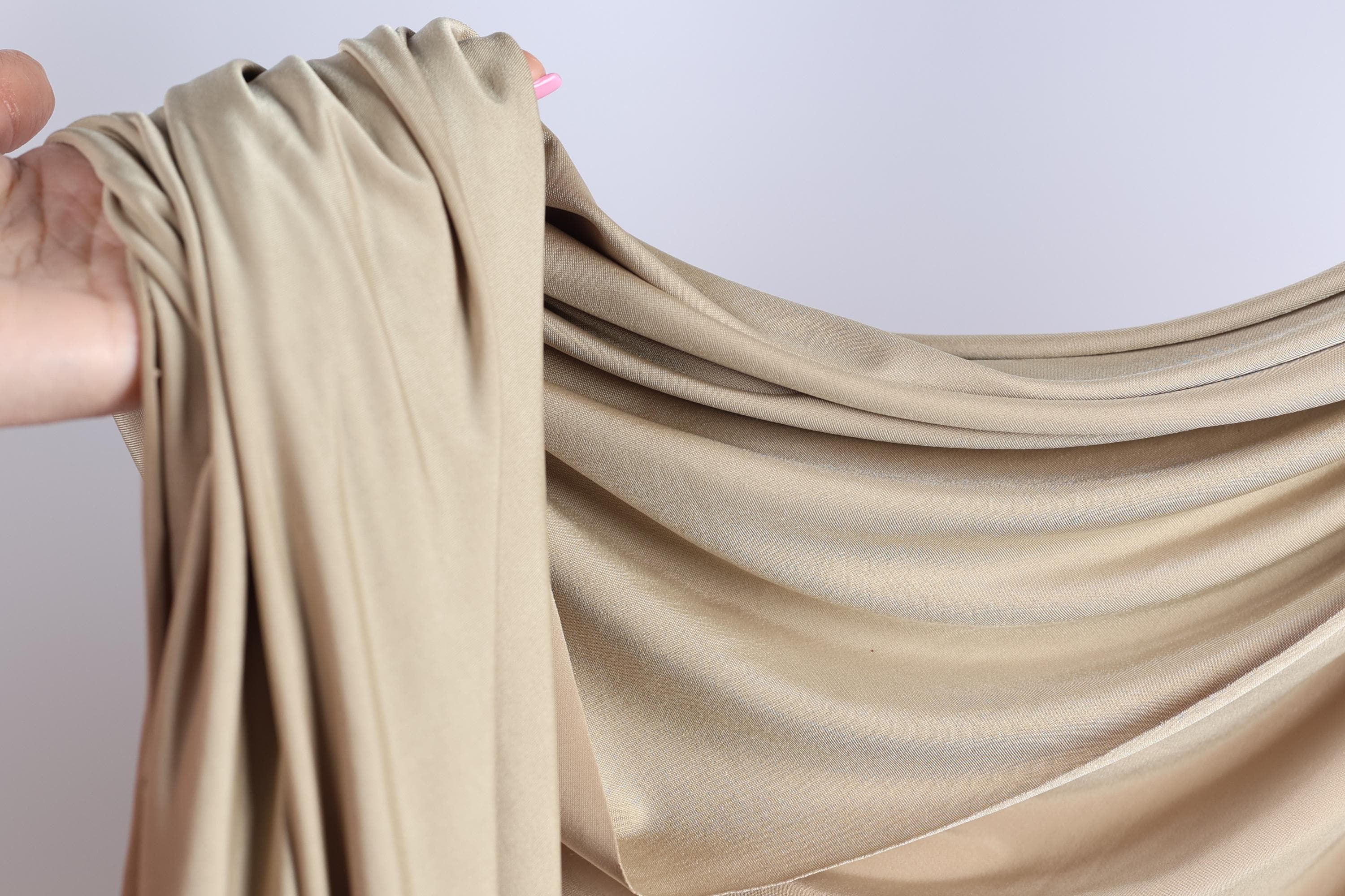 A hand is holding a piece of light brown fabric, which appears to be a type of chiffon or sheer material.