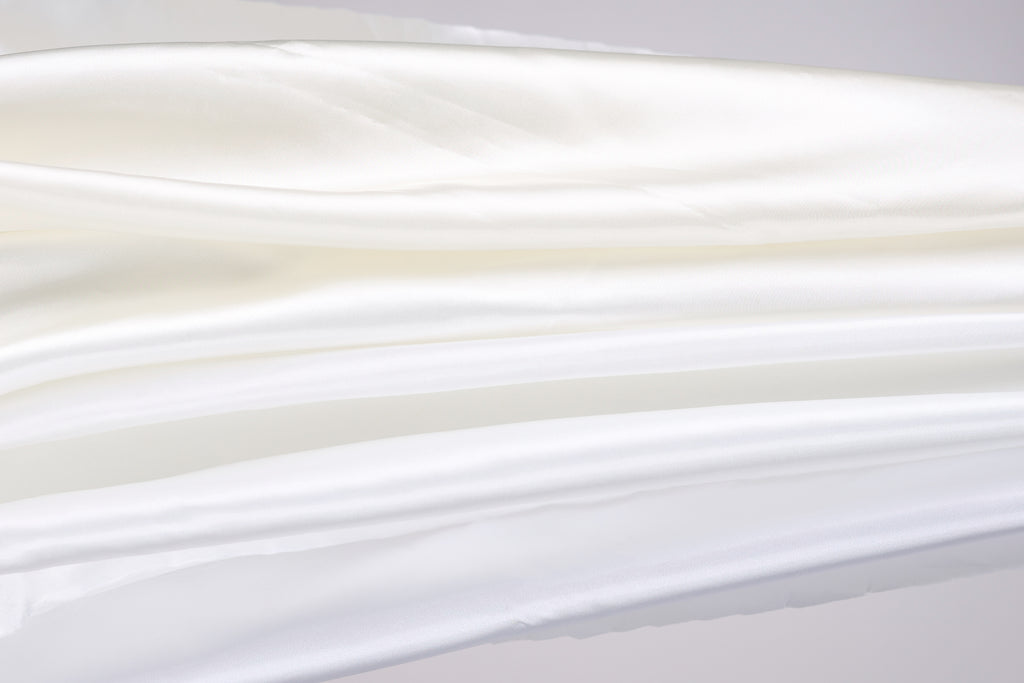 The image is a close-up of a white fabric, possibly silk or chiffon, with a soft, flowing texture.