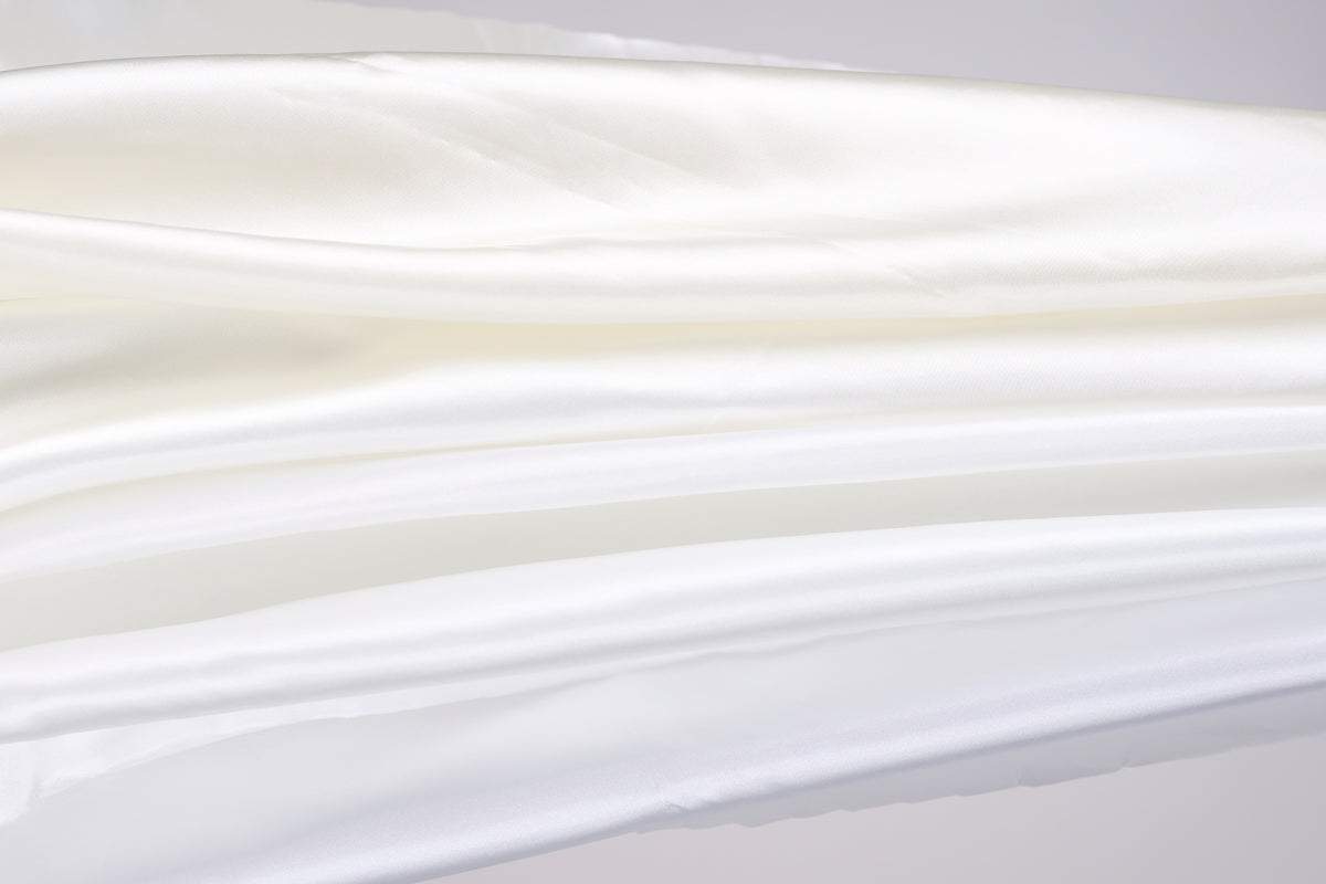 The image is a close-up of a white fabric, possibly silk or chiffon, with a soft, flowing texture.