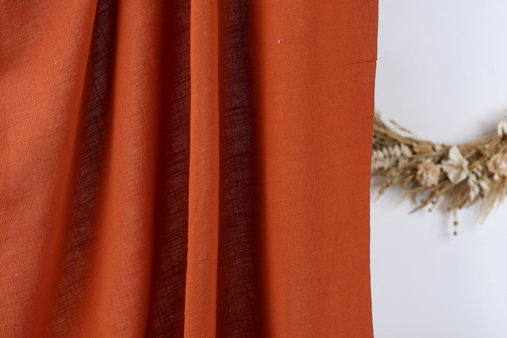 a close-up view of a red fabric, possibly a curtain or a piece of clothing, with a wreath of dried flowers or branches placed next to it on a white wall.