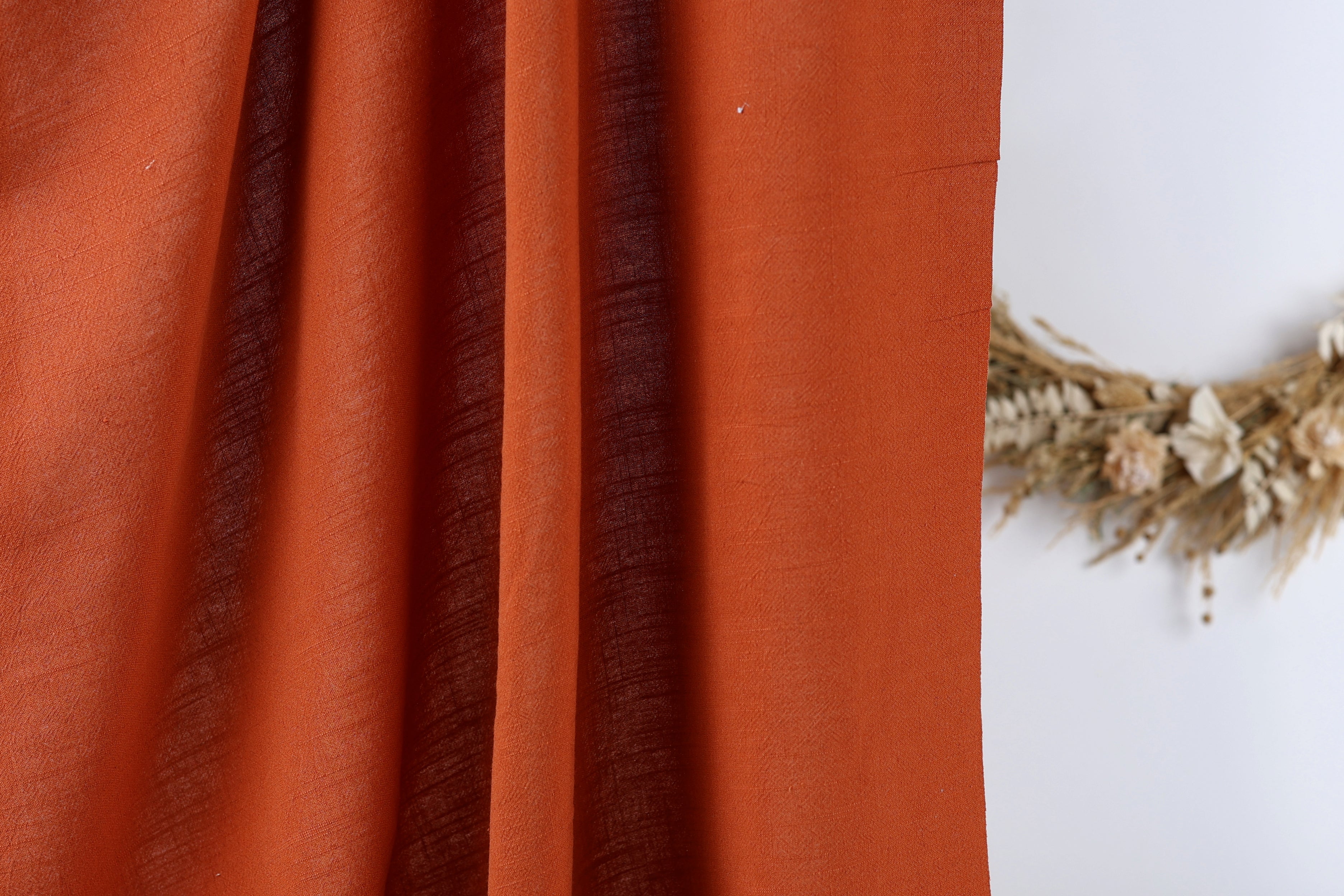 a close-up view of a red fabric, possibly a curtain or a piece of clothing, with a wreath of dried flowers or branches placed next to it on a white wall.