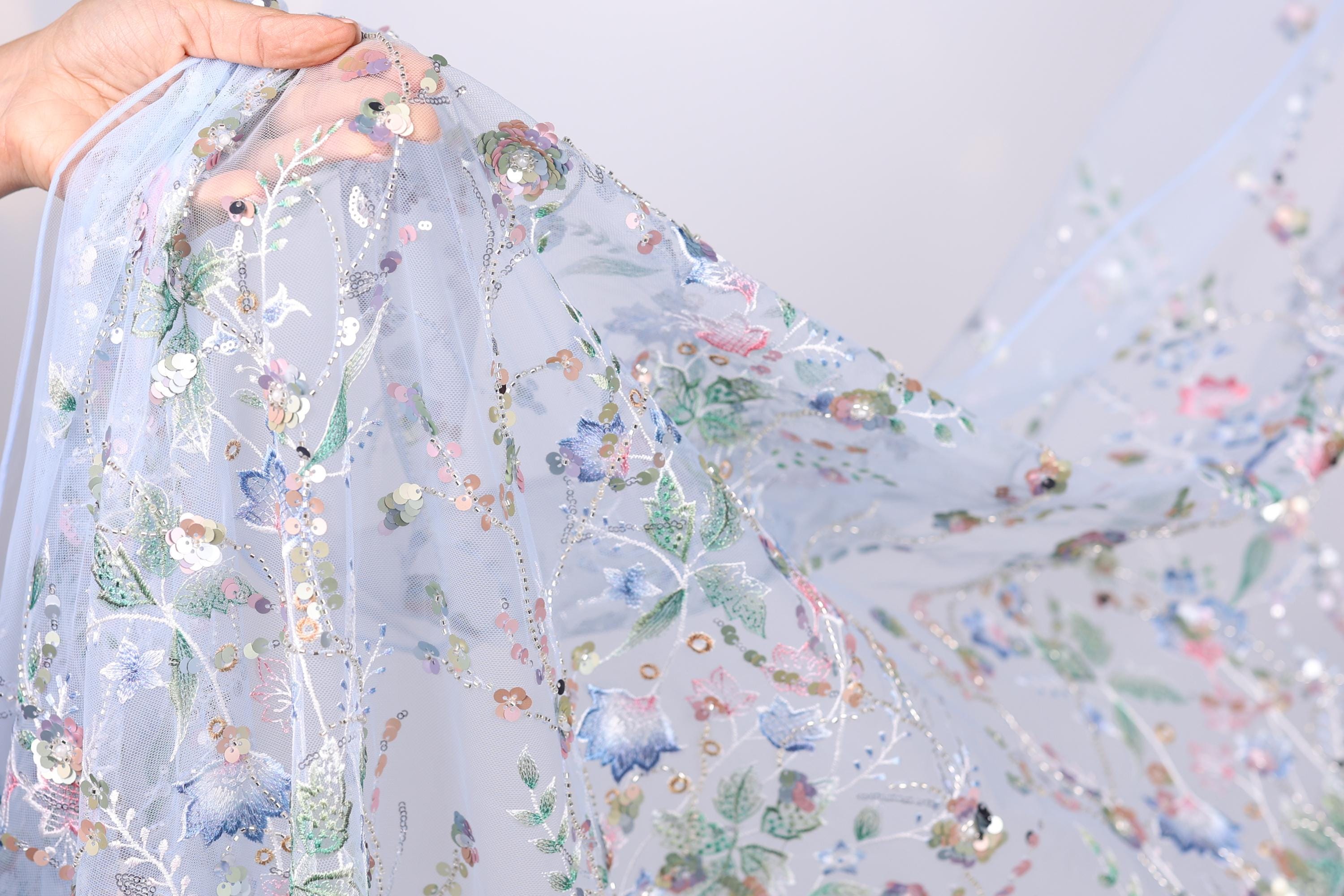 A hand is holding a piece of fabric with a floral pattern, featuring various colors and designs.