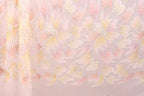 a close-up view of a fabric with a repeating pattern of pink and yellow flowers or leaves. The pattern is intricate and detailed, with the flowers or leaves appearing to be made of a shiny material, possibly sequin or glitter. The fabric has a soft and delicate appearance, suggesting it could be used for clothing or home decor.