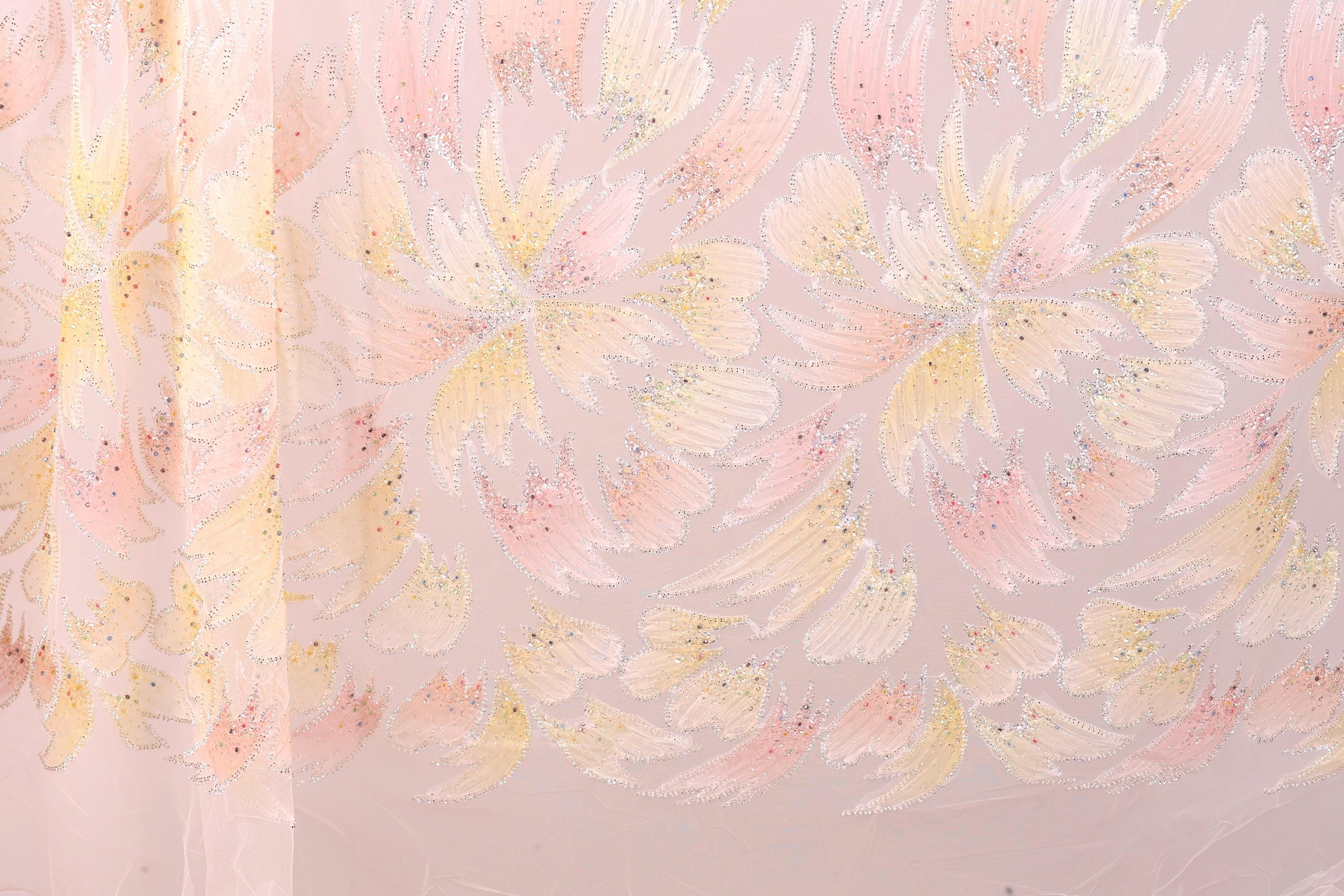 a close-up view of a fabric with a repeating pattern of pink and yellow flowers or leaves. The pattern is intricate and detailed, with the flowers or leaves appearing to be made of a shiny material, possibly sequin or glitter. The fabric has a soft and delicate appearance, suggesting it could be used for clothing or home decor.