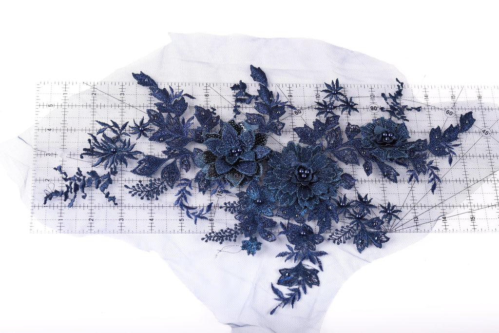 a collection of blue floral embroidery pieces, including flowers and leaves, arranged on a transparent surface.