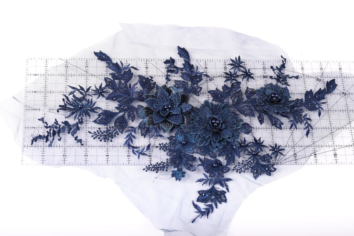 a collection of blue floral embroidery pieces, including flowers and leaves, arranged on a transparent surface.