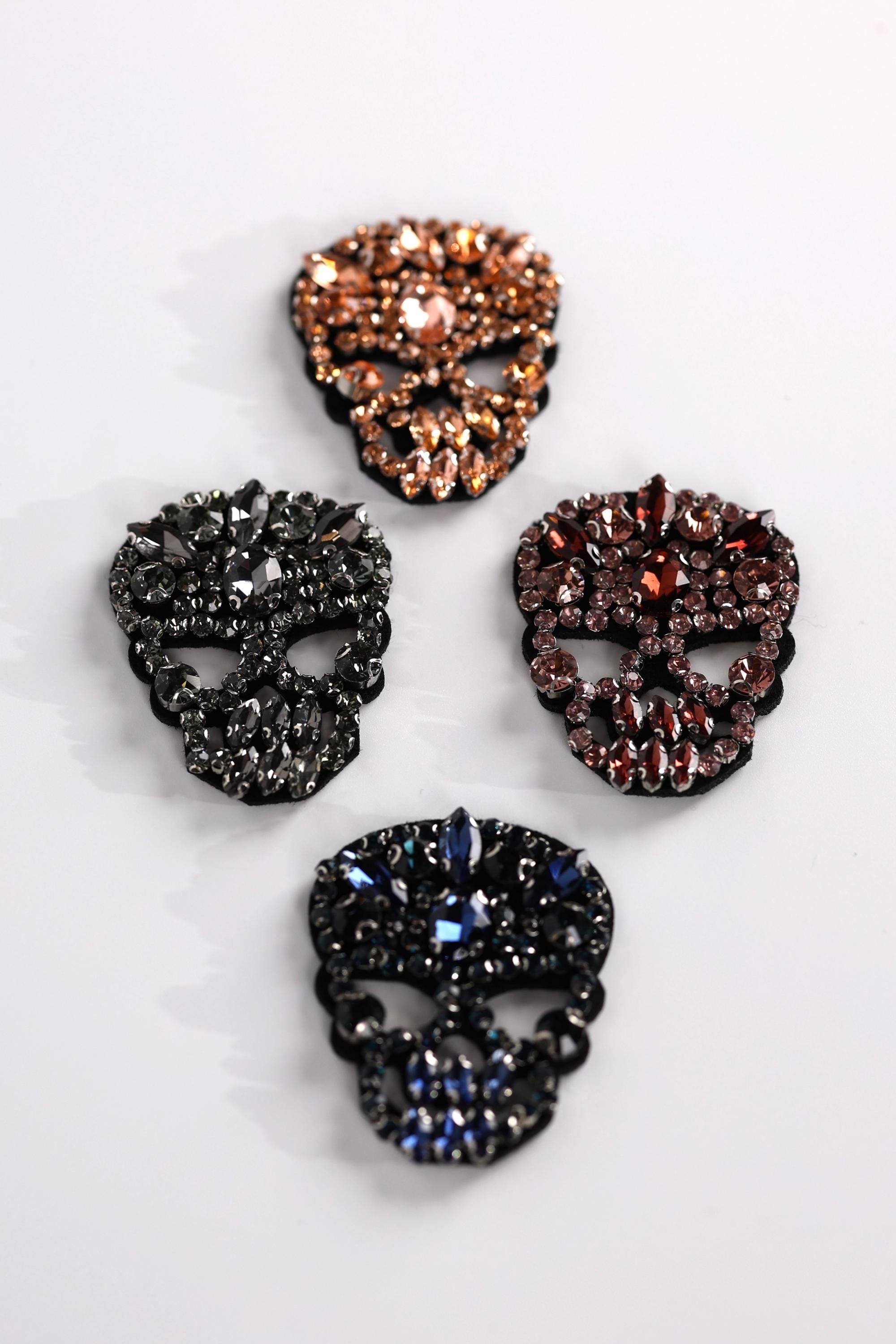 four ornate skull-shaped brooches, each adorned with a variety of colorful gemstones or crystals.