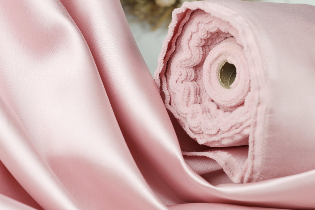 A close-up view of a soft, pink satin fabric, possibly silk or satin, with a visible crease and a small hole in the center.