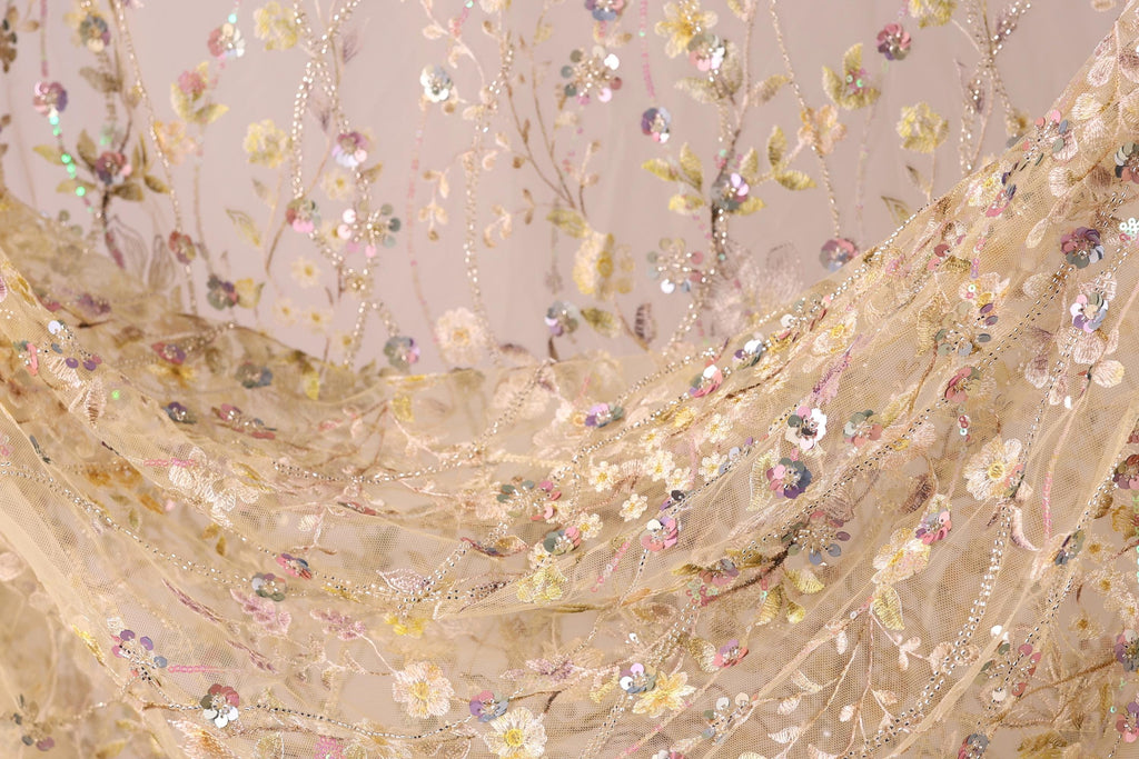 a close-up view of a delicate, intricately embroidered fabric with a floral pattern. The fabric appears to be made of sheer material, giving it a soft and delicate appearance. The embroidery is detailed and colorful, with various shades of pink, yellow, and green creating a vibrant and eye-catching design. The fabric is spread out, showcasing the full extent of the embroidered pattern and its intricate design.